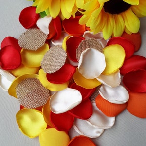 Può includere: Assortimento di petali di fiori in tessuto di colore rosso, arancione, giallo e bianco. I petali sono sparsi su una superficie bianca. Ci sono anche piccoli pezzi di tessuto di juta nel mix.