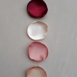 May include: Five fabric rose petals in different shades of red, pink, and beige. The petals are arranged vertically from darkest to lightest.