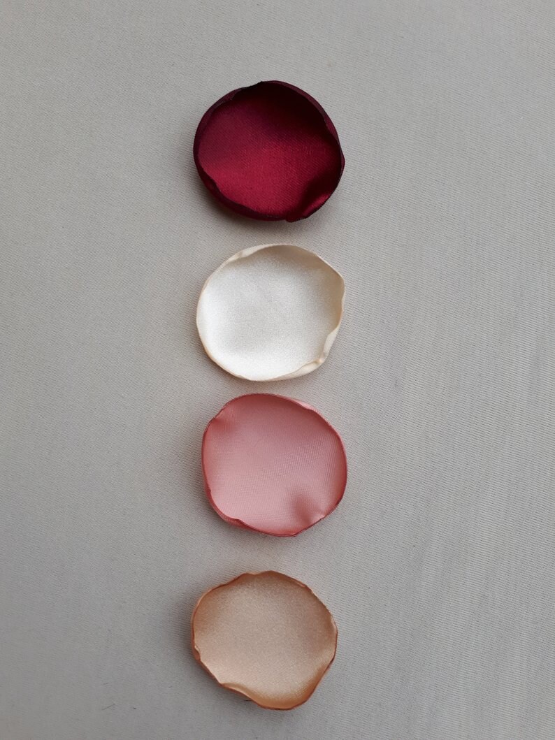 May include: Five fabric rose petals in different shades of red, pink, and beige. The petals are arranged vertically from darkest to lightest.