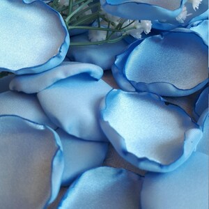 May include: A collection of light blue satin rose petals. The petals are arranged in a pile on a white surface.