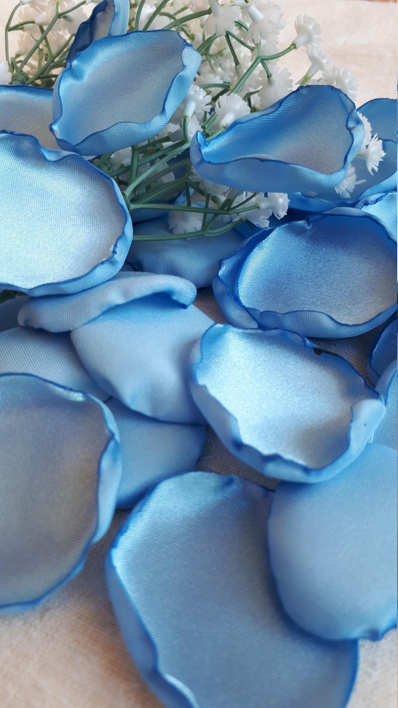May include: A collection of light blue satin rose petals. The petals are arranged in a pile on a white surface.