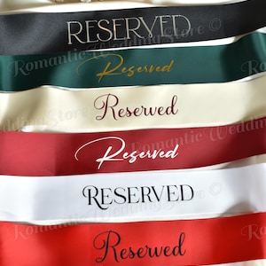 May include: A collection of six satin ribbons in black, dark green, cream, burgundy, white, and red. Each ribbon features the word Reserved printed in a distinct font style, including serif, script, and elegant lettering, arranged horizontally.