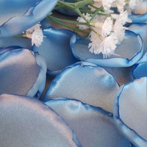 May include: A pile of light blue satin rose petals with white flowers scattered on top.