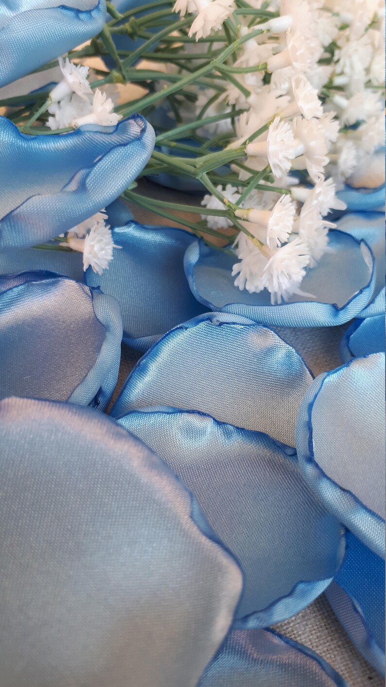 May include: A pile of light blue satin rose petals with white flowers scattered on top.