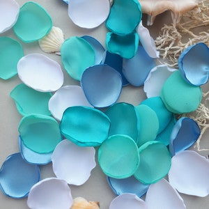 以下が含まれることがあります： 青、ターコイズ、白の色の布製のフラワーペタルの詰め合わせ。ペタルは薄い灰色の表面に散らばっています。