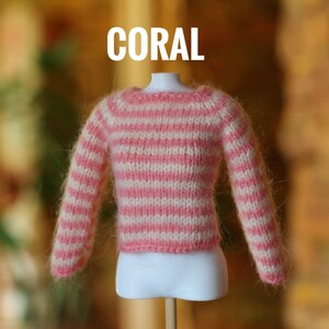 May include: A coral and white striped sweater displayed on a mannequin. The sweater has long sleeves and a round neckline. The word "CORAL" is written in white block letters above the sweater.