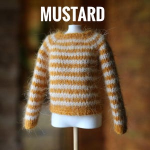 May include: A miniature mustard-colored sweater with white horizontal stripes. The sweater is displayed on a white mannequin bust. The word "MUSTARD" is printed in white at the top of the image. The sweater has long sleeves and a round neckline.