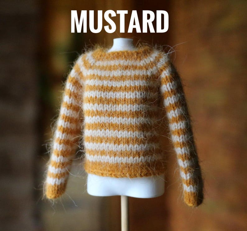 May include: A miniature mustard-colored sweater with white horizontal stripes. The sweater is displayed on a white mannequin bust. The word "MUSTARD" is printed in white at the top of the image. The sweater has long sleeves and a round neckline.