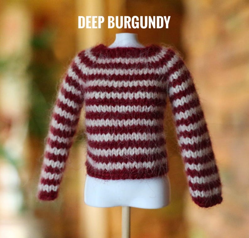 May include: A miniature burgundy and white striped sweater. The sweater is displayed on a white mannequin and has long sleeves. The text "DEEP BURGUNDY" is displayed above the sweater. The sweater is made of a fuzzy material.