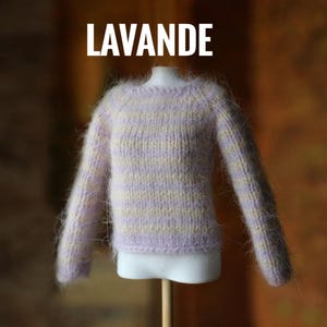 May include: A lavender and cream-colored knit sweater with long sleeves. The word "LAVANDE" is displayed in white block letters above the sweater. The sweater is displayed on a white mannequin torso.