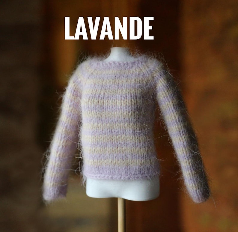 May include: A lavender and cream-colored knit sweater with long sleeves. The word "LAVANDE" is displayed in white block letters above the sweater. The sweater is displayed on a white mannequin torso.