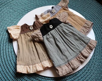 May include: Three short-sleeved dresses featuring a solid-colored bodice with a small white flower-shaped button at the neckline. The sleeves and bottom hem are made of a light beige fabric with a dark polka dot pattern and ruffled edges.