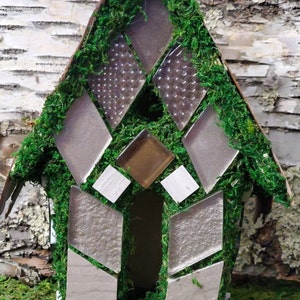 May include: A small, moss-covered house made of wood and glass. The house has a diamond-shaped window and is decorated with small, white tiles.