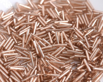 May include: A pile of rose gold glass beads, each bead is a long cylinder shape.