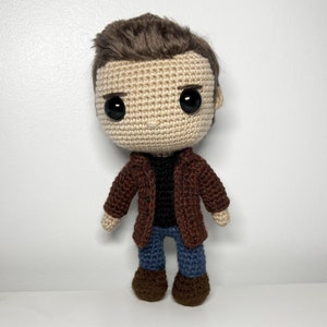 May include: A crocheted doll with brown hair, a brown jacket, blue jeans, and brown shoes.