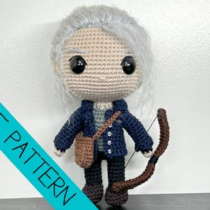 May include: Crocheted doll of a character with grey hair, wearing a navy blue jacket, grey shirt, black trousers, and brown boots. The doll has a brown satchel and a brown bow and arrow. The text "PDF PATTERN" is on a teal diagonal stripe.