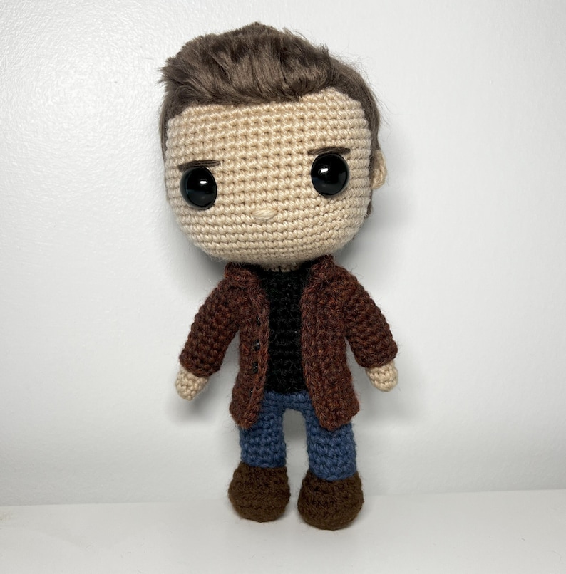 May include: A crocheted doll with brown hair, a brown jacket, blue jeans, and brown shoes.