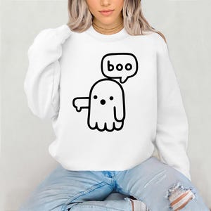 以下が含まれることがあります： 白いスウェットシャツに、黒い漫画の幽霊が「boo」と書かれた吹き出しをつけています。