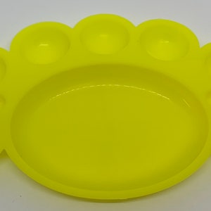May include: A yellow plastic paint palette with seven individual wells for mixing paint. The palette is shaped like a paw print.
