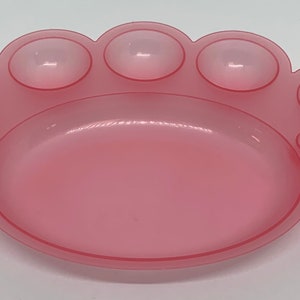 May include: A pink plastic paint palette with seven round wells. The palette is shaped like a paw print.