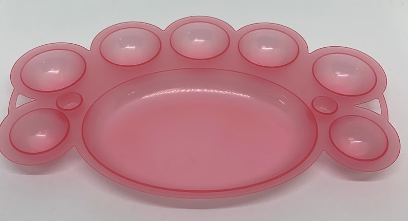 May include: A pink plastic paint palette with seven round wells. The palette is shaped like a paw print.
