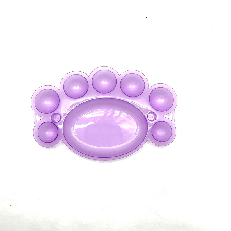 May include: A purple plastic paint palette with seven round wells and a large oval well in the center.