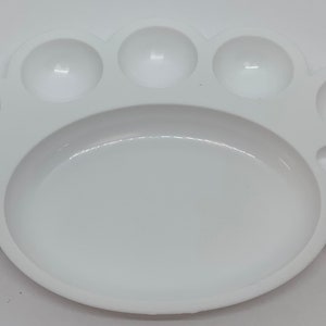 May include: White plastic paint palette with nine circular wells for mixing paint. The palette has a large oval area in the center.