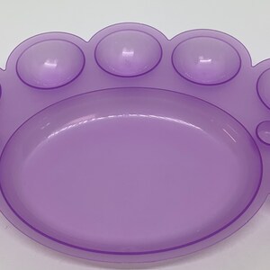 May include: A purple plastic paint palette with nine wells, including a large central well and eight smaller wells around the edge.