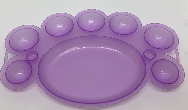 May include: A purple plastic paint palette with nine wells, including a large central well and eight smaller wells around the edge.