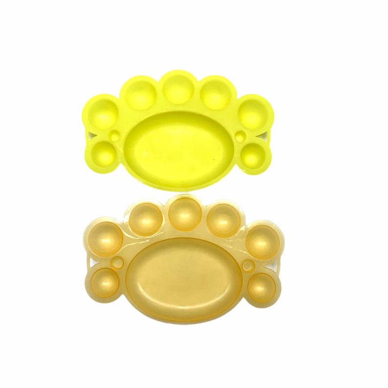 May include: Two paint palettes, one yellow and one gold, with multiple circular wells for mixing paint.