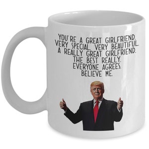 May include: White ceramic coffee mug with a black and white image of a man with a red tie and thumbs up. The text on the mug reads "You're a great girlfriend. Very special. Very beautiful. A really great girlfriend. The best really. Everyone agrees. Believe me."