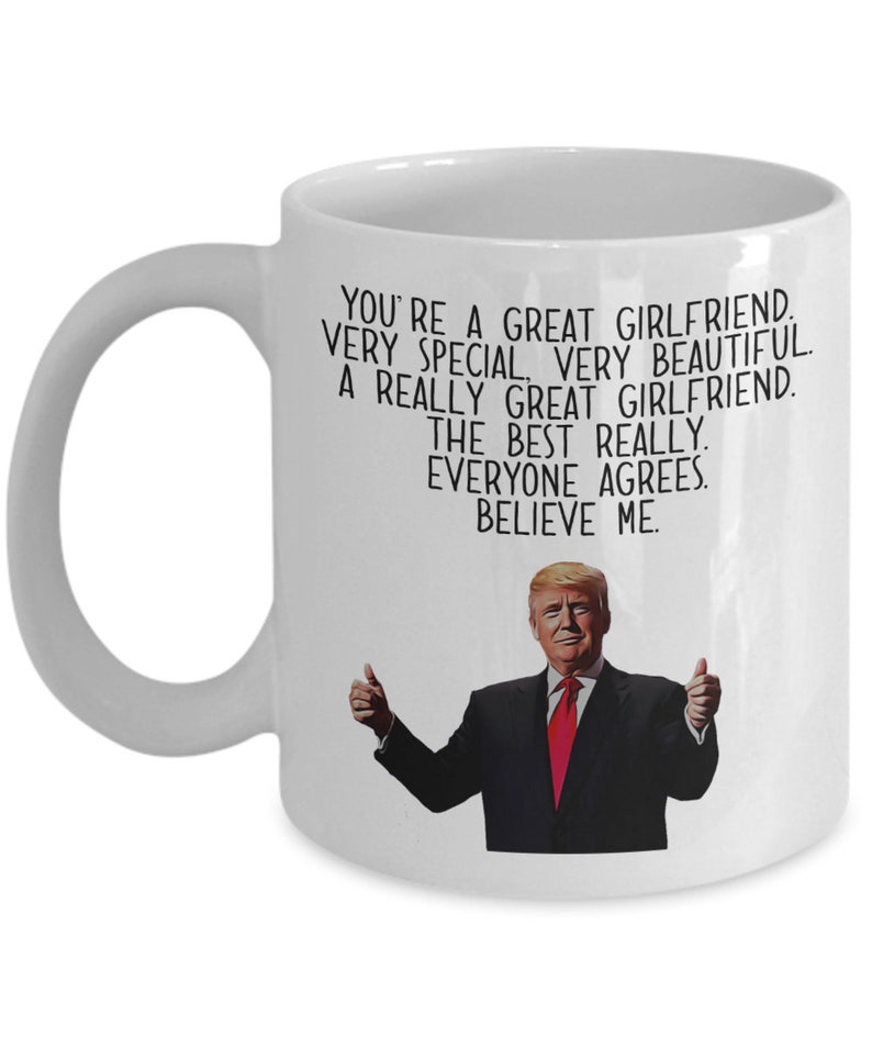 May include: White ceramic coffee mug with a black and white image of a man with a red tie and thumbs up. The text on the mug reads "You're a great girlfriend. Very special. Very beautiful. A really great girlfriend. The best really. Everyone agrees. Believe me."