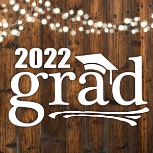 Op de afbeelding: Een rustieke houten achtergrond met een string witte lampjes. De tekst "2022 grad" is in wit geschreven met een afstudeerhoed boven het woord "grad".