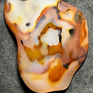 Può includere: Una pietra di agata bianca, marrone e nera con un motivo a spirale unico. La pietra è liscia e lucidata e ha una forma naturale e organica.