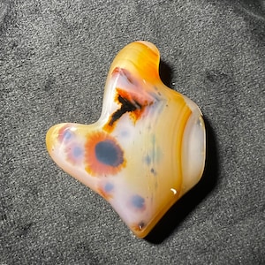 Può includere: Una pietra di agata levigata e liscia con un motivo astratto unico di marrone, bianco e arancione. La pietra ha una forma naturale e organica.