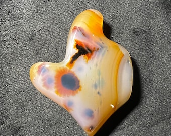 May include: A smooth, polished agate stone with a unique, abstract pattern of brown, white, and orange. The stone has a natural, organic shape.