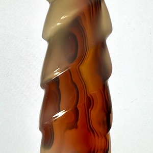 Può includere: Una pietra di agata marrone e bianca con un motivo a spirale. La pietra ha la forma di una torre alta e sottile.