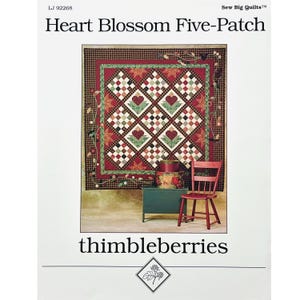 May include: A quilt pattern titled "Heart Blossom Five-Patch" by thimbleberries. The quilt features a central design of hearts and floral patterns in red, green, and white. The image includes a red chair and a green cabinet.