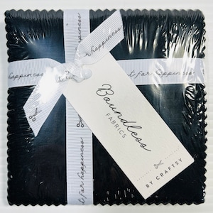 May include: A package of black fabric squares with a white ribbon tied around them. The ribbon has the text "It's for happiness" printed on it. The package is labeled "Boundless Fabrics by Craftsy".