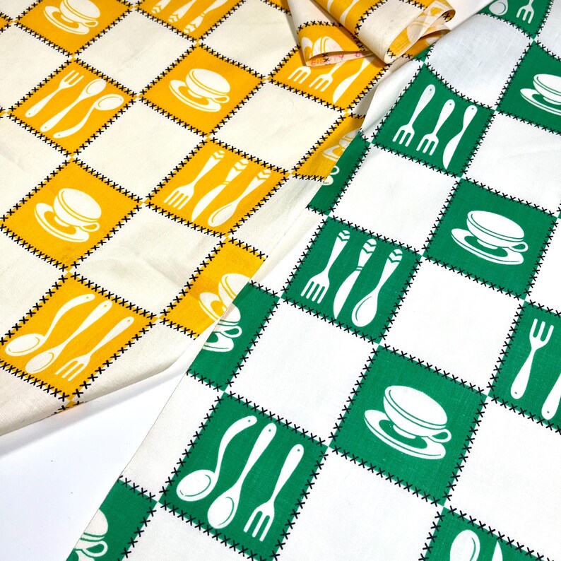 May include: Two pieces of fabric featuring a checkered pattern with black cross-stitch borders. One piece has yellow squares with white illustrations of cups, saucers, forks, and spoons. The other piece has green squares with white illustrations of cups, saucers, forks, and spoons.