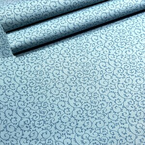 May include: Light blue fabric with a repeating pattern of swirling vines and leaves. Several rolls of the fabric are visible, showcasing the design. The fabric has a subtle texture and a soft, muted color palette.