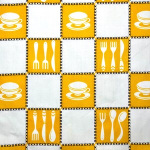 May include: A white and yellow checkered pattern fabric featuring repeating images of teacups, forks, knives, and spoons. The fabric has a stitched border and is suitable for kitchen or dining decor.