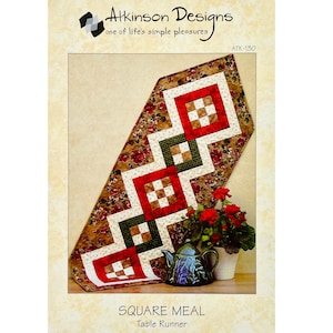 May include: A quilting pattern for a table runner called "Square Meal". The pattern features a geometric design with red, green, white, and brown squares. The pattern is shown on a table runner with a floral print background.
