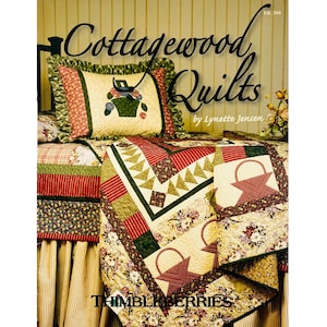 May include: A bed covered with a patchwork quilt and pillow featuring floral and basket designs. The quilt has red, green, and cream-colored sections. The text "Cottagewood Quilts" and "Thimbleberries" are visible.