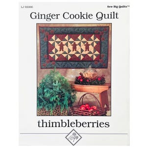 May include: Ginger Cookie Quilt pattern by Thimbleberries. The pattern features a quilt design with gingerbread men and red hearts. The quilt is displayed on a wall with a Christmas-themed vignette below.