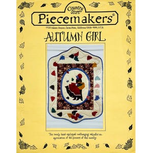May include: A yellow poster with the text "Country Store Piecemakers" and "Autumn Girl." The poster features a framed wall hanging with a central image of a figure in a red dress and a basket, surrounded by leaves and floral patterns.