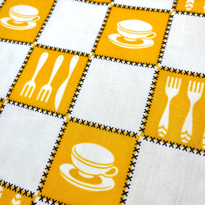 May include: A close-up of a white and yellow checkered tablecloth. The yellow squares feature white illustrations of coffee cups, forks, and knives. The squares are outlined with black stitching, creating a vintage, retro aesthetic.