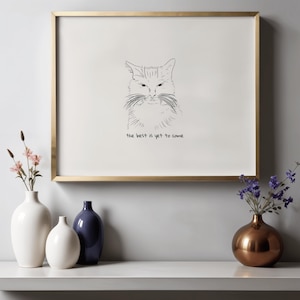 Könnte beinhalten: Ein gerahmter Druck mit goldfarbenem Rahmen zeigt eine Skizze eines Katzenkopfes. Der Text "the best is yet to come" steht darunter. Der Druck wird über einem weißen Regal mit Vasen und Blumen ausgestellt.