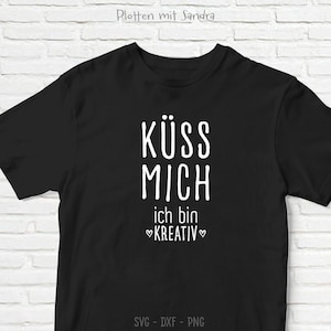 May include: Black t-shirt with white text that reads "KÜSS MICH ich bin KREATIV" in a bold, sans-serif font. The shirt also has the text "SVG - DXF - PNG" at the bottom. The shirt is a casual wear item.