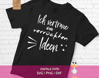 Könnte beinhalten: Ein schwarzes T-Shirt mit kurzen Ärmeln und dem weißen Schriftzug Ich vertraue auf meine verrückten Ideen, ergänzt durch drei kleine Herzen und ein grafisches Element. Am Kragen hängt ein braunes Etikett mit dem Text Plotten mit Sandra.